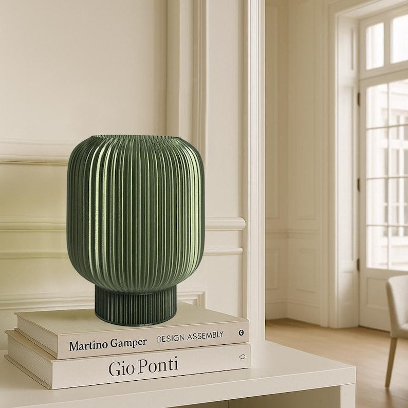 Green ribbed vase on books in a room with a window