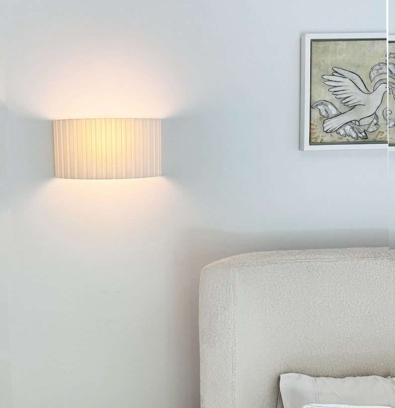 Light fixture on a wall next to a bed with a decorative pillow.