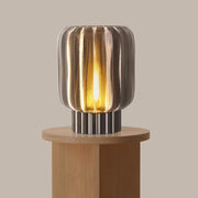Decorative lamp with striped design on a wooden pedestal against a beige background